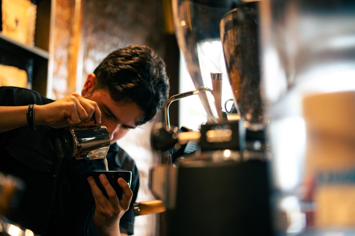 Barista concentrado despejando leite em xícara de café