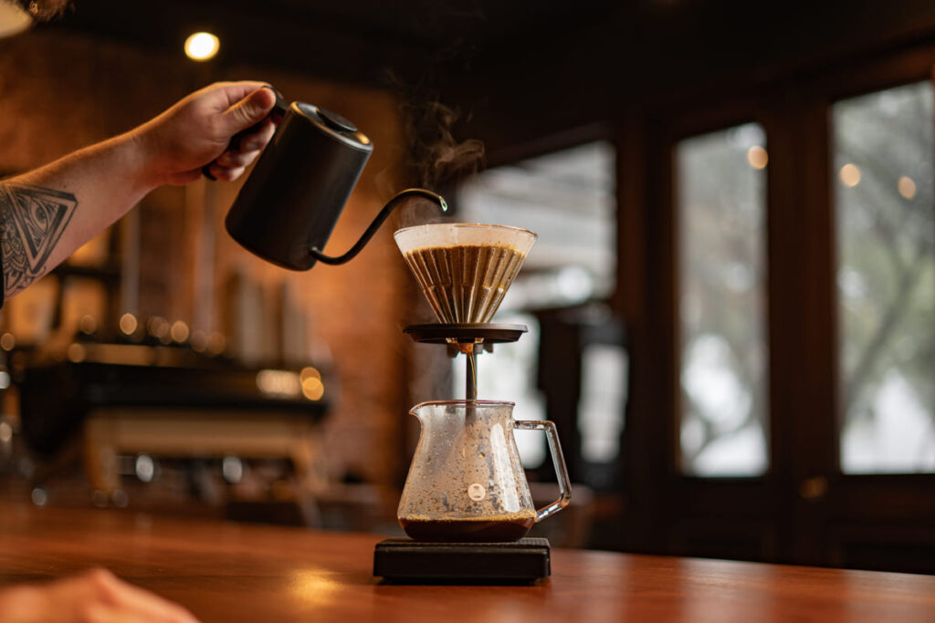 Mão segurando bule que derrama água em coador de café